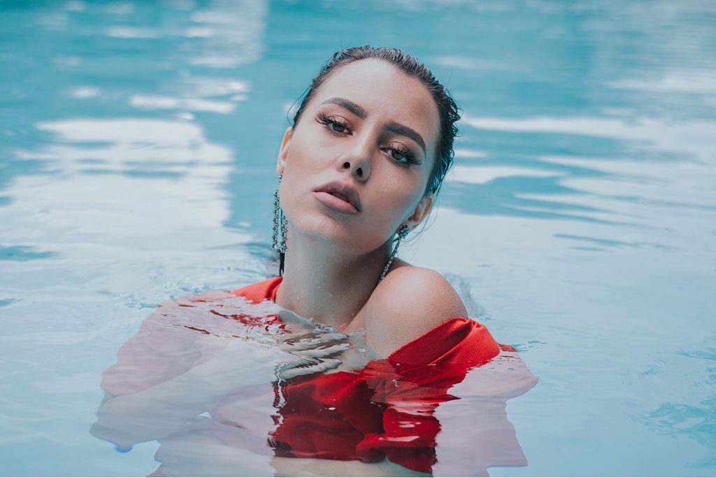 A gorgeous Florida entertainer in a red top cooling off in a bright blue swimming pool.